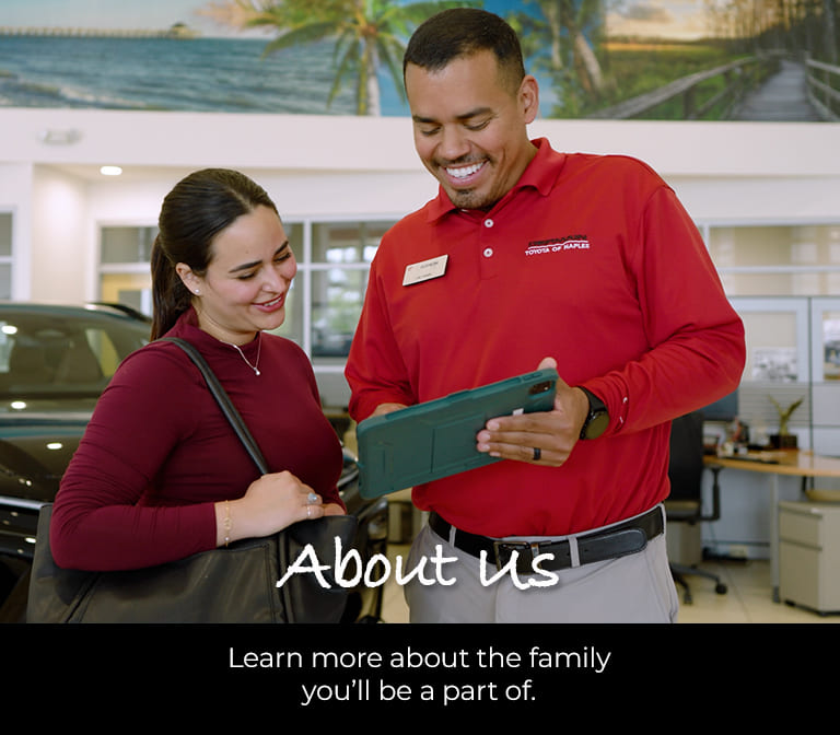 Germain Toyota of Naples employee showing a customer information on a tablet in the dealership showroom. Text reads: "About Us – Learn more about the family you'll be a part of."